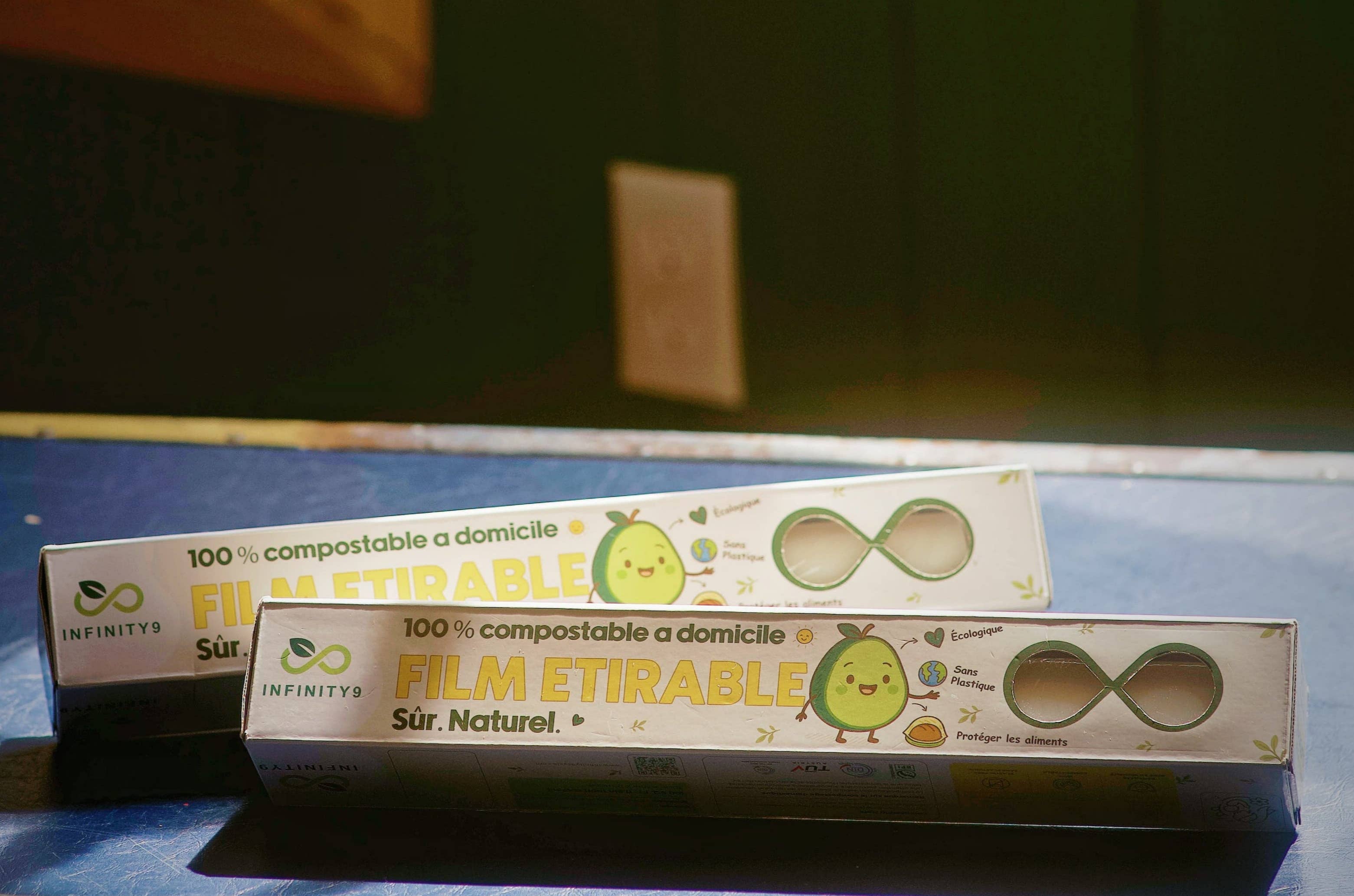 Two rolls of eco-friendly infinity9 cling wrap on a table surface with a green wall and window. 