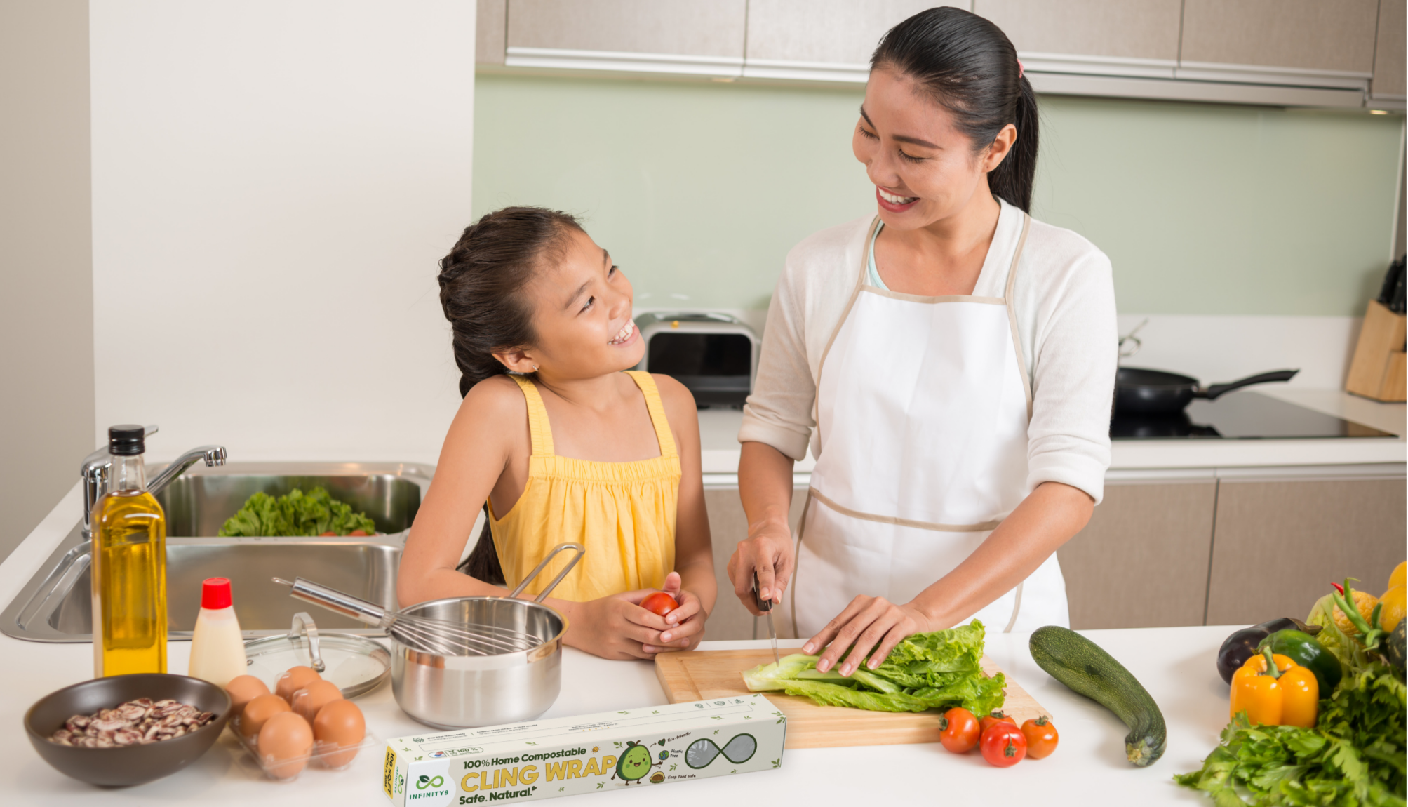 Mother and Daugther in the kitchen with produce cutting, cleaning, with Infinity9 cling food wrap and smiling. family.