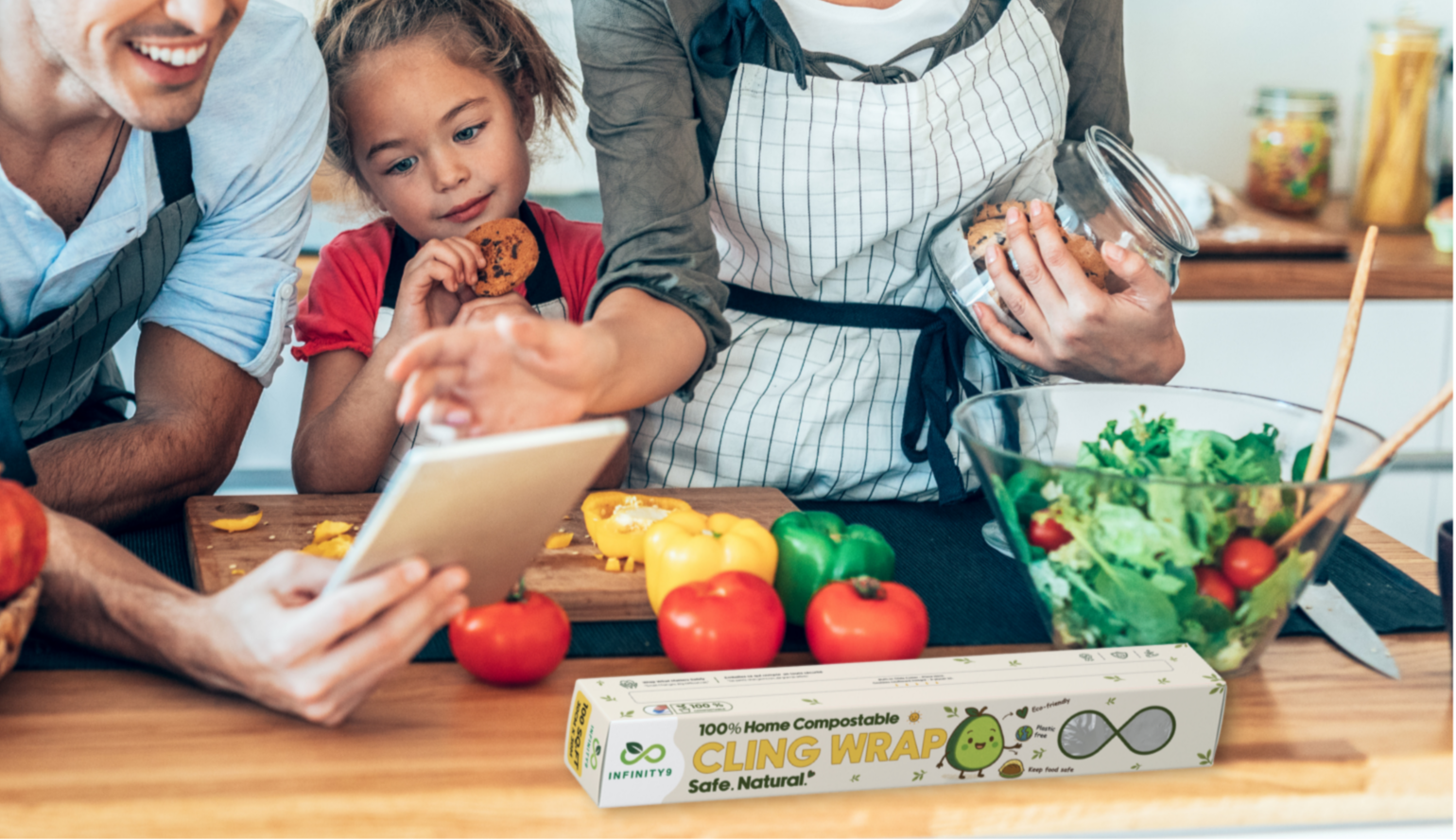 Family in a kitchen preparing food with a tablet, Infinity9 cling compostable eco-friendly wrap, surrounded by fresh vegetables.