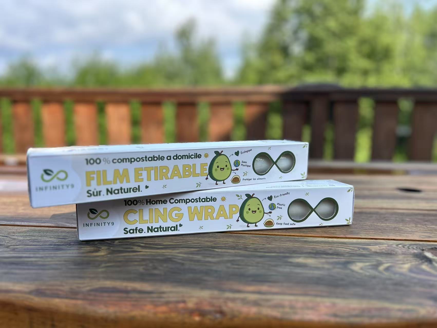 Two packages of Infinity9 home compostable cling wrap on a wooden surface with a blurred natural background